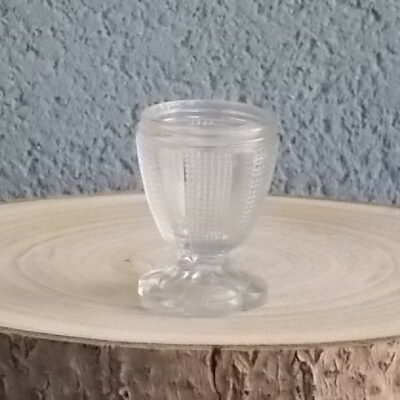 Coquetier à pied en verre épais translucide soufflé moulé. Décors alterné de bande lisse et double stries. Pied en quartier formant fleur.