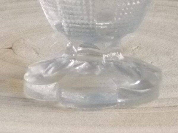 Coquetier à pied en verre épais translucide soufflé moulé. Décors alterné de bande lisse et double stries. Pied en quartier formant fleur.