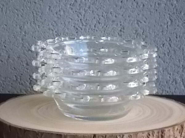 Coupelle ronde en verre translucide à bordure plate ajourée, moulé pressé. Coté biaisé, fond effet martelé avec motif forme de la coupelle.