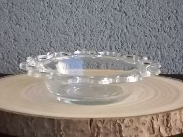 Coupelle ronde en verre translucide à bordure plate ajourée, moulé pressé. Coté biaisé, fond effet martelé avec motif forme de la coupelle.