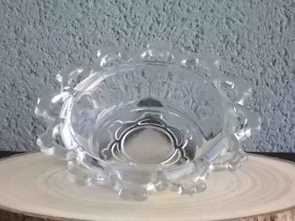 Coupelle ronde en verre translucide à bordure plate ajourée, moulé pressé. Coté biaisé, fond effet martelé avec motif forme de la coupelle.