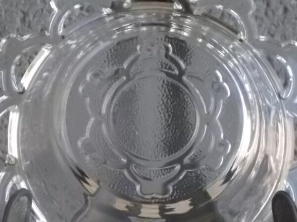 Coupelle ronde en verre translucide à bordure plate ajourée, moulé pressé. Coté biaisé, fond effet martelé avec motif forme de la coupelle.