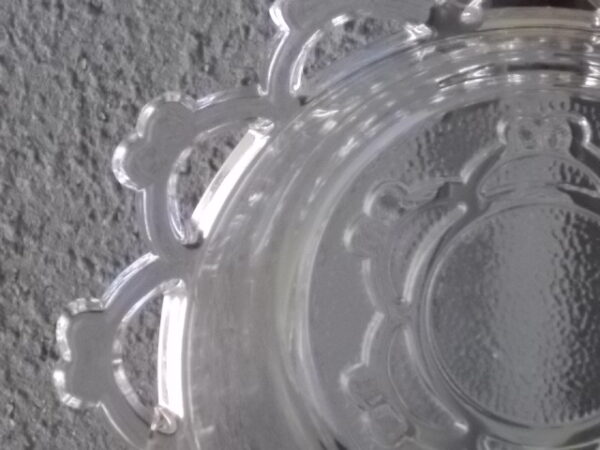 Coupelle ronde en verre translucide à bordure plate ajourée, moulé pressé. Coté biaisé, fond effet martelé avec motif forme de la coupelle.