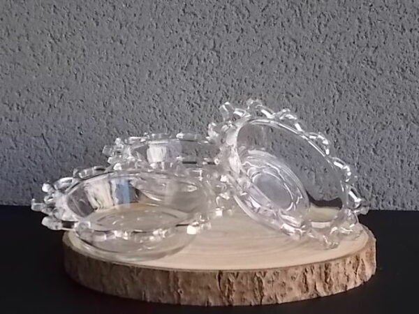 Coupelle ronde en verre translucide à bordure plate ajourée, moulé pressé. Coté biaisé, fond effet martelé avec motif forme de la coupelle.