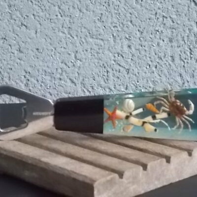 Décapsuleur manche en Résine avec inclusion de Coquillages, Etoile de Mer, Crabe, plantes aquatiques et Paillettes. En Inox 18/8 de la Marque Acero