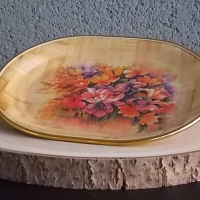 Petit plateau ovale creux, en tissage de feuille de Palmier vernissé, à décors imprimé fleurie. Bordure en cerclage de plastique Doré.