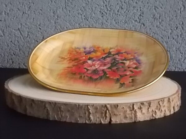 Petit plateau ovale creux, en tissage de feuille de Palmier vernissé, à décors imprimé fleurie. Bordure en cerclage de plastique Doré.