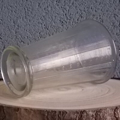 Verre doseur en verre épais translucide moulé pressé. Forme évasé sur base socle. Verre gradué contenant 300 gr. De Portieux Mougin Déposé.