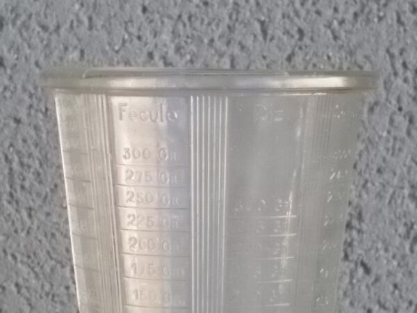 Verre doseur en verre épais translucide moulé pressé. Forme évasé sur base socle. Verre gradué contenant 300 gr. De Portieux Mougin Déposé.