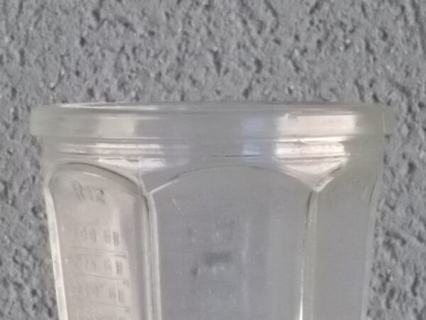 Verre doseur en verre translucide épais moulé. Forme évasé à cotes plates sur base socle Hexagonale. Graduation extérieur, et rebord épais.