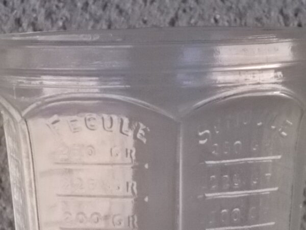 Verre doseur en verre translucide épais moulé. Forme évasé à cotes plates sur base socle Hexagonale. Graduation extérieur, et rebord épais.